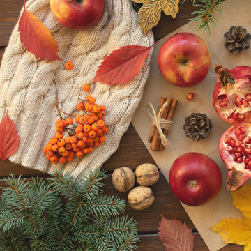 Apples, pomegranate, cinnamon, cones, walnuts, fallen leaves on a wooden background. Autumn composition.