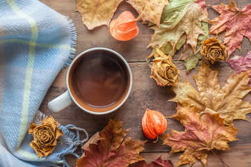 Top view orange coffee Cup in the frame of the autumn colored maple leaves on the brown wooden background from boards
