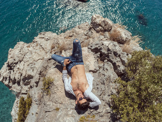 Traveler on the rocks near the sea laying on rock. Summer Travel Vacation. Handsome young caucasian tourist man in casual clothes outdoors on the nature. Wide angle photo on fish eye lens
