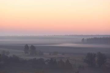 Serene autumn landscape. Clear sky and dense mist with trees in distanse