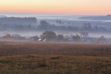 Autumn serene landscape. Fields and distant trees in mist at sunrise copyspace