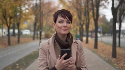 stylish young woman uses smartphone against background of autumn street