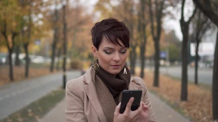 stylish young woman uses smartphone against background of autumn street