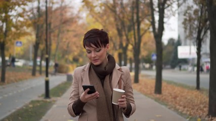 stylish woman walking in autumn city with phone in her hands