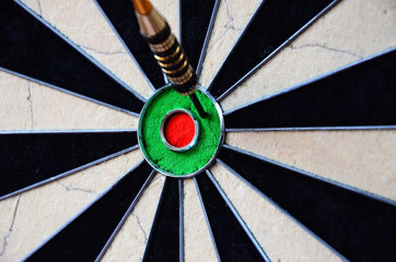 Dart arrow hitting in the target center of dartboard.