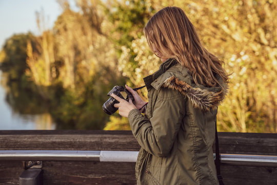 Young woman is standing on a bridge and checking picture previews on the camera display