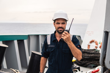 Marine Deck Officer or Chief mate on deck of vessel or ship . He holds VHF walkie-talkie radio in...