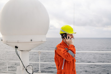 Marine Deck Officer or seaman on deck of vessel or ship . He is speaking on the mobile cell phone