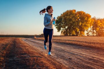 Vrouw loopt in herfst veld bij zonsondergang. Gezond levensstijlconcept. Actieve sportieve mensen