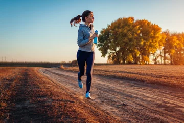 Fototapete Joggen Frau, die bei Sonnenuntergang auf dem Herbstgebiet läuft. Gesundes Lebensstilkonzept. Aktive sportliche Menschen