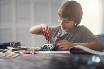 Pleasant work. Cheerful enthusiastic boy using pliers and smiling while fixing the details in his...