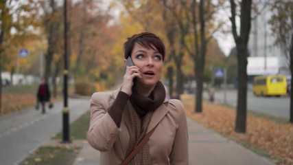 stylish woman is having fun talking on phone on background of autumn city