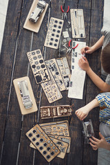 Unusual activity. Two boys sitting at the table covered with various wooden details and making mechanisms out of their constructor
