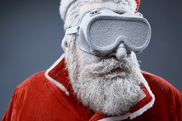 Close up portrait of bearded old man in Santa costume covered with snow. He is wearing protective...