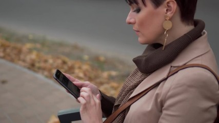 stylish female uses phone on bench and looks into camera