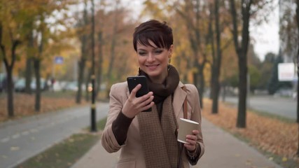 stylish woman walking in autumn city with phone in her hands