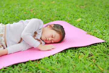 Little Asian child girl sleeping on pink mattress in green grass lawn at summer park garden.