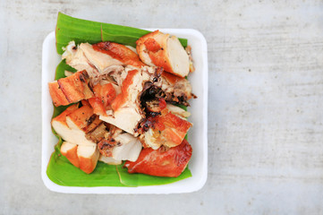 Grilled chicken with chopped on banana leaf in a tray against cement table with copy space. Top view.