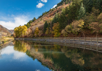 Fototapeta na wymiar Lake lined by fence and fall foliage trees and hill