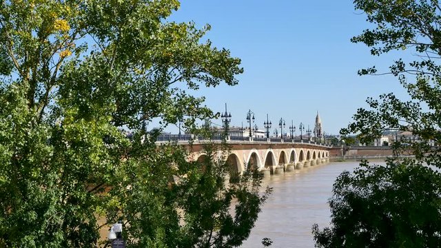 View of the Pont de Pierre (stone bridge) behind the tree in the city center of Bordeaux, in southwestern France. The river is the Garonne. Filmed in october 2018 during a sunny day. Blue sky.