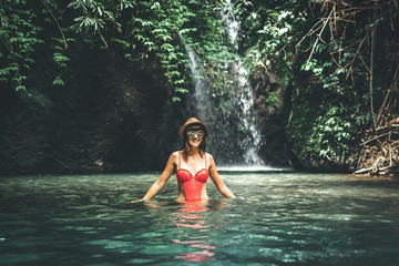 Fototapeta premium Young woman tourist with straw hat in the deep jungle with waterfall. Real adventure concept. Bali island.