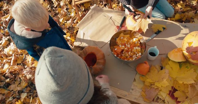Caucasian family - mother with 2 kids - daughter and son, carving pumpkins for Halloween on the table outdoors in the backyard. 4K UHD 60 FPS