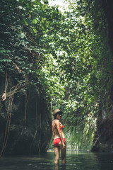 Rear view of young woman tourist with straw hat and red swimsuit in the deep jungle. Real adventure concept. Bali island.