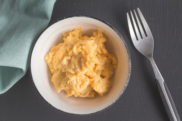 Moist scrambled eggs in bowl on black rustic table - Top view close up photo