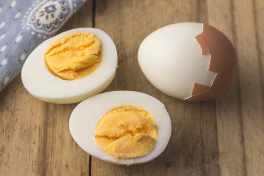 Boiled eggs isolated on rustic wooden table - hardboiled egg sliced and one with peeled shell
