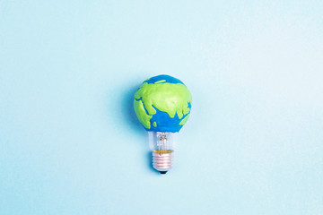 Light bulb with plasticine Earth planet model on blue background. Global ecology, International Day...