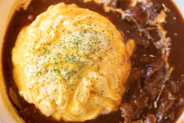 Japanese Omu rice (Omelette or egg) on top with Demi-glace sauce or Curry sauce on white plate over wooden table