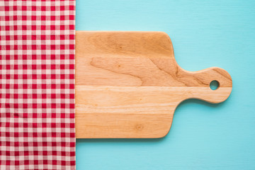 Top view of unused brand new brown handmade wooden cutting board and red napkins on blue wooden table background - Food and kitchen concept