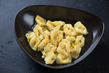 Black bowl with tortellini in bouillon, studio shot over black stone background, selective focus