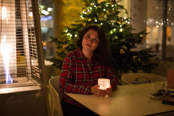 Holiday, Christmas and people concept - Young woman sitting in cafe near Christmas tree background at night