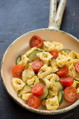Tortellini with addition of roasted cherry tomatoes and zucchini in a serving pan, vertical shot