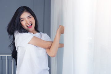Woman stretching in bed after waking up, back view. Woman sitting near the big white window while stretching .she happy and smile.