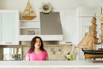 Hobby, emotions and collecting concept - young surprised woman looking to layout of a sailboat in the kitchen