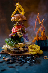 Tasty smoked grilled and glazed beef burger with lettuce, cheese and bacon served with french fries on wooden table with copyspace, smoke mesquite timber wood in background.