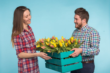 Happy florists fixing tulips in a big wooden box on blue background