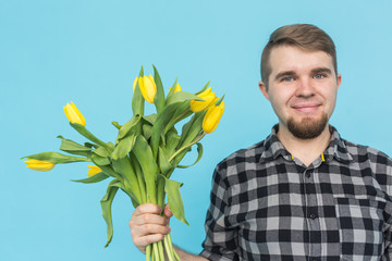 Man with bouquet of yellow tulips. Yellow tulips in the hands of a bearded man on blue background