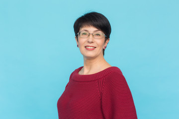 Middle-aged charming woman in red sweater posing on blue background