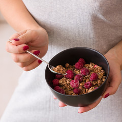 Closeup of a girl holding a black bowl with organic granola with coconut milk and raspberries.