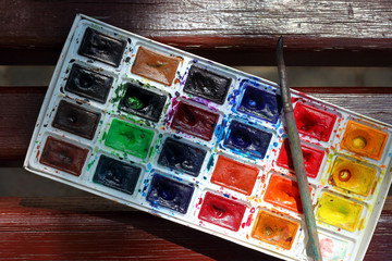 Palette with watercolor paints and brush lying on the wooden background