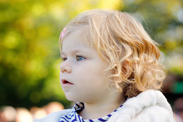 Fototapeta premium Portrait of little cute toddler girl sitting in stroller or pram and going for a walk. Happy cute baby child having fun outdoors.