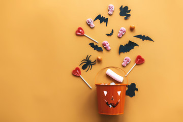 Halloween Jack o Lantern bucket with holiday candy, bats,spiders, skulls on orange paper, flat lay....