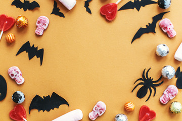 Halloween frame flat lay on orange paper. Holiday candy border with bats, spiders, skulls top view. Trick or treat. Halloween background. Season's greeting card mockup