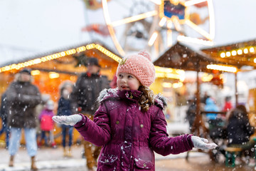 Little cute kid girl having fun on traditional German Christmas market during strong snowfall.....