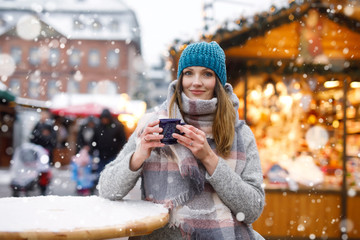 Beautiful young woman drinking hot punch, mulled wine on German Christmas market. Happy girl in...