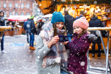 Happy kid girl and young beautiful woman with cup of steaming hot chocolate and mulled wine....
