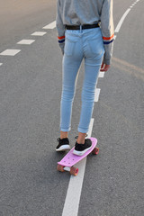 Teenage girl wearing gray shirt and jeans riding skateboard or penny board on asphalt street back view. Outdoor activities and healthy lifestyle concept.